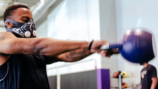 man lifting kettlebell with training mask