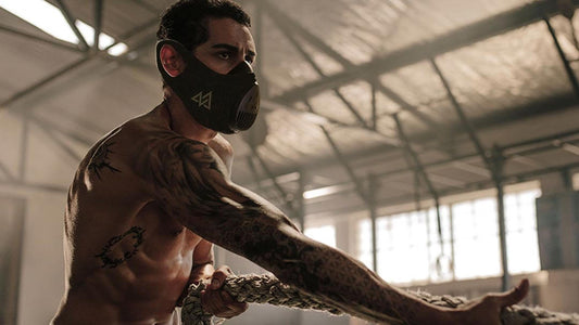 Man training in gym setting with mask on pulling a rope